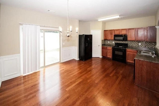 kitchen with brown cabinetry, dark countertops, dark wood-type flooring, black appliances, and a sink