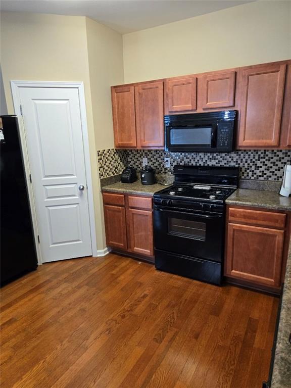 kitchen with dark countertops, black appliances, backsplash, and dark wood-style flooring