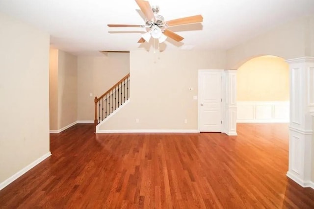 empty room with arched walkways, wood finished floors, stairs, and a ceiling fan