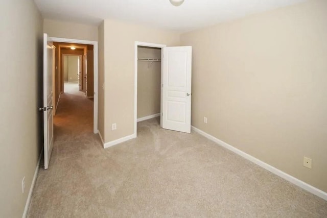 unfurnished bedroom with a closet, light colored carpet, and baseboards