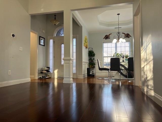 foyer featuring ornate columns, dark hardwood / wood-style flooring, ornamental molding, a notable chandelier, and a tray ceiling