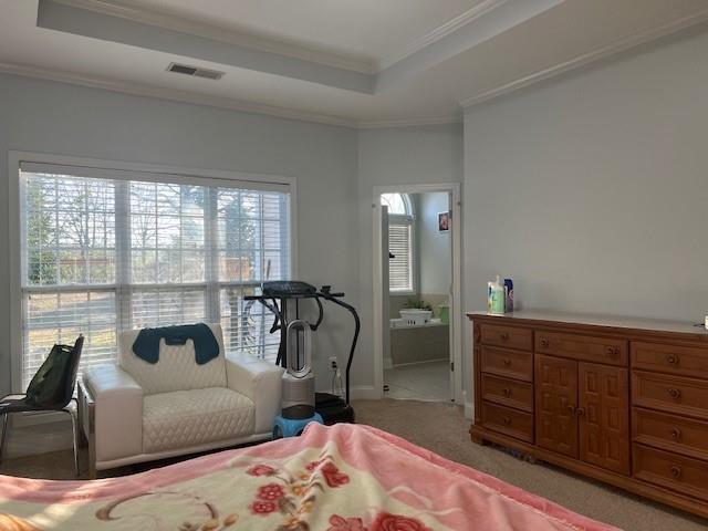 bedroom with crown molding, a tray ceiling, light colored carpet, and ensuite bathroom