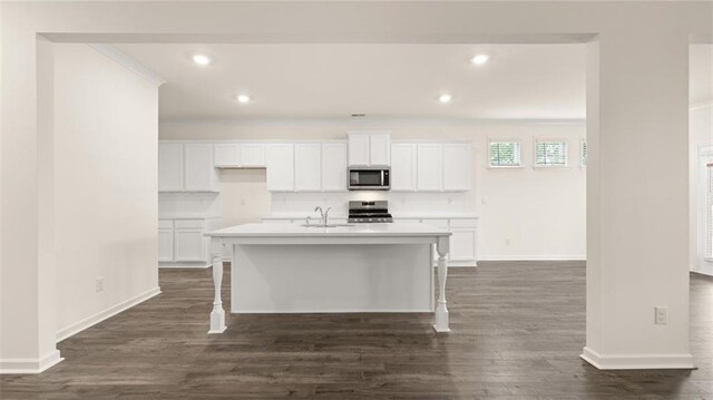 kitchen featuring range, an island with sink, a kitchen bar, dark hardwood / wood-style flooring, and white cabinets