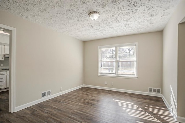 unfurnished room with visible vents, baseboards, and dark wood-style flooring