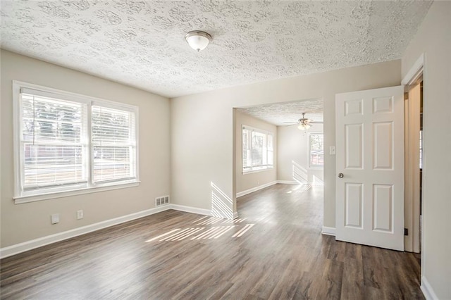 empty room featuring visible vents, a textured ceiling, dark wood-style floors, baseboards, and ceiling fan