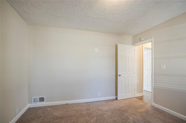 carpeted spare room with baseboards, visible vents, and a textured ceiling