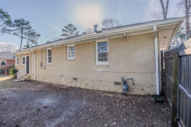 view of property exterior with crawl space, entry steps, brick siding, and fence