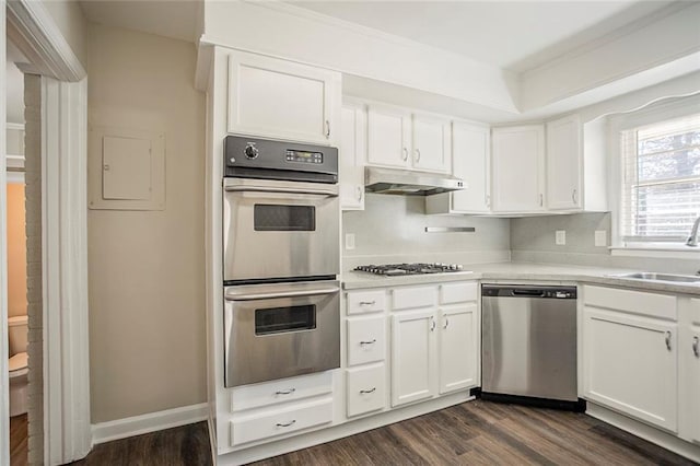 kitchen featuring dark wood-style floors, a sink, white cabinets, under cabinet range hood, and appliances with stainless steel finishes