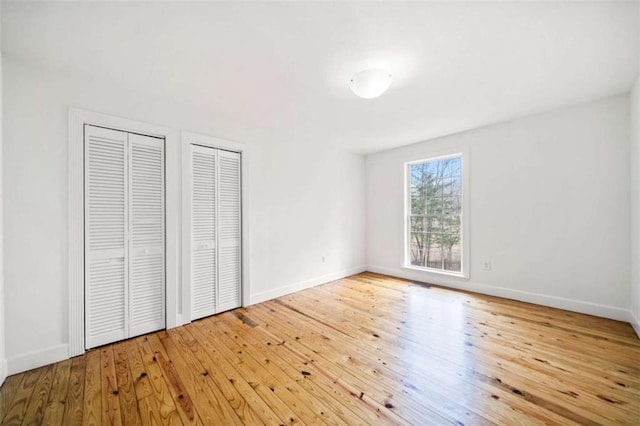 unfurnished bedroom with two closets and light hardwood / wood-style floors