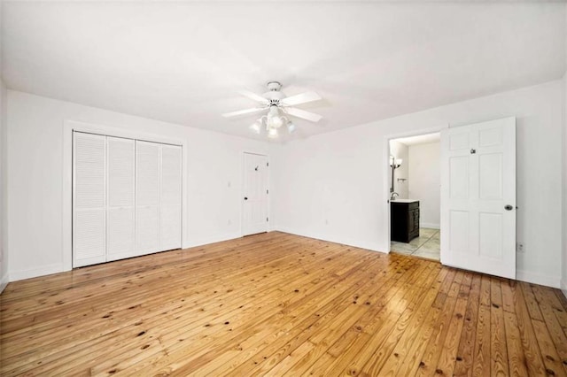 unfurnished bedroom featuring multiple closets, ensuite bath, ceiling fan, and light hardwood / wood-style flooring