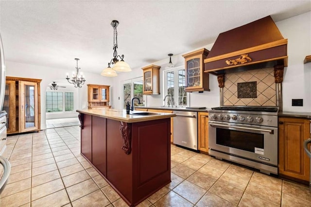 kitchen with premium range hood, sink, hanging light fixtures, appliances with stainless steel finishes, and a kitchen island with sink