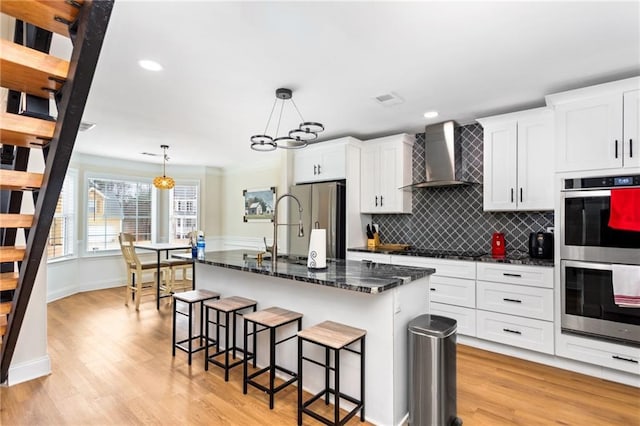 kitchen featuring a breakfast bar area, appliances with stainless steel finishes, light wood-type flooring, decorative backsplash, and wall chimney exhaust hood