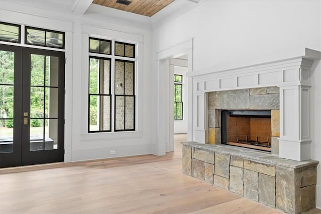 interior space featuring beamed ceiling, french doors, light hardwood / wood-style flooring, and a stone fireplace