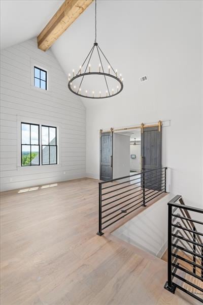 staircase with an inviting chandelier, a barn door, beamed ceiling, high vaulted ceiling, and hardwood / wood-style flooring