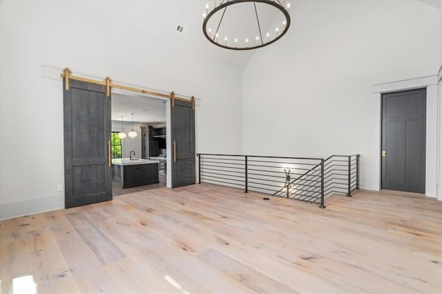 unfurnished living room with a barn door, light hardwood / wood-style floors, high vaulted ceiling, and sink