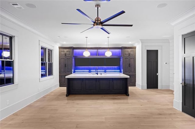 kitchen featuring dark brown cabinets, ceiling fan, ornamental molding, and a kitchen island with sink