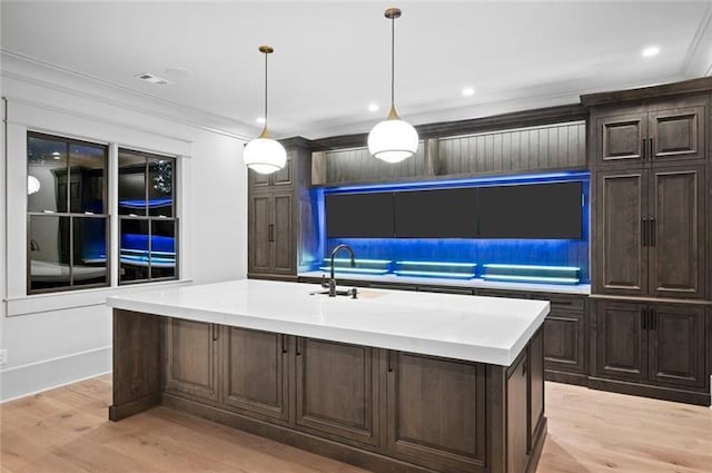 kitchen featuring light wood-type flooring, ornamental molding, a kitchen island with sink, sink, and hanging light fixtures