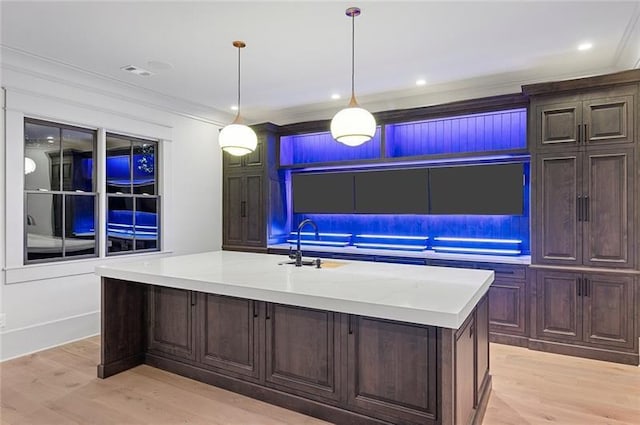 kitchen featuring a kitchen island with sink, crown molding, and decorative light fixtures