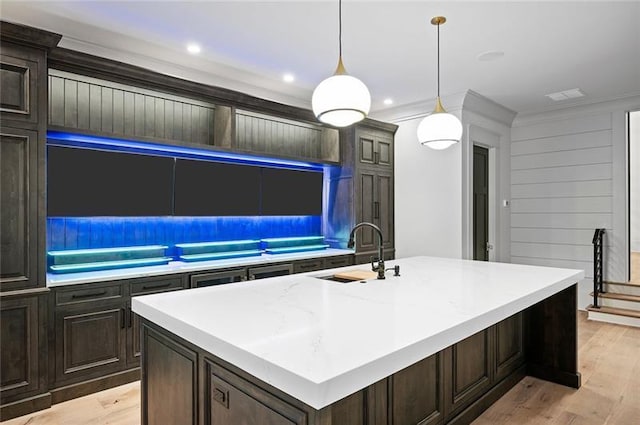 kitchen featuring dark brown cabinetry, sink, decorative light fixtures, a kitchen island with sink, and light wood-type flooring