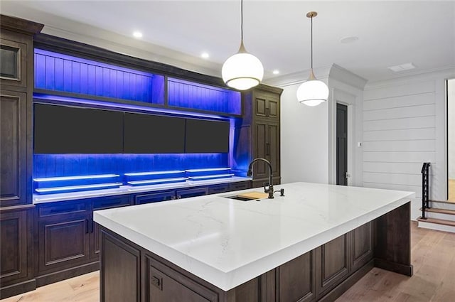 kitchen featuring light stone counters, sink, pendant lighting, a center island with sink, and light hardwood / wood-style flooring