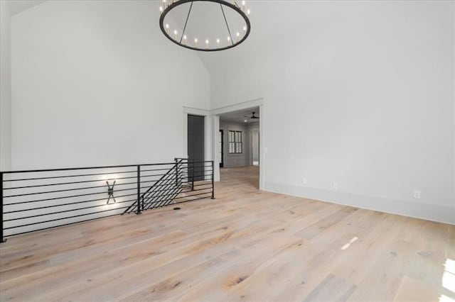 empty room featuring high vaulted ceiling, light hardwood / wood-style floors, and ceiling fan with notable chandelier