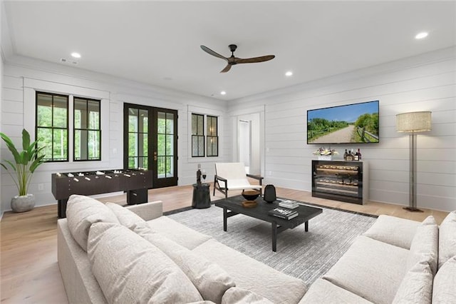 living room with ceiling fan, french doors, light hardwood / wood-style floors, and wood walls