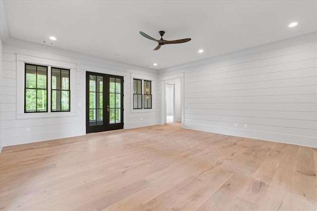 unfurnished living room featuring french doors, light hardwood / wood-style flooring, ceiling fan, and wood walls