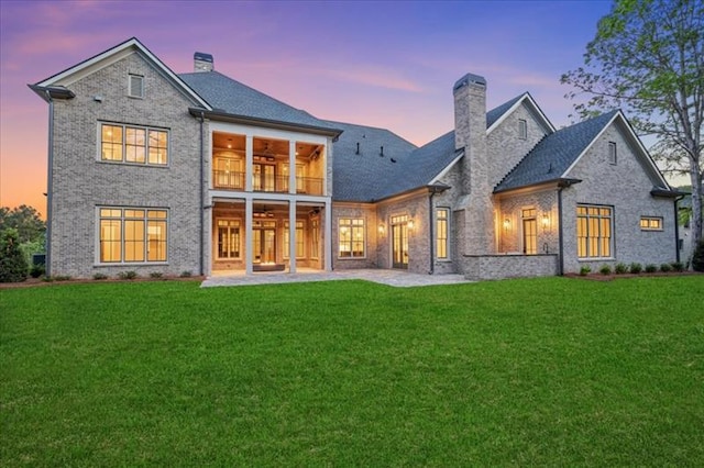 back house at dusk with a balcony, ceiling fan, and a lawn