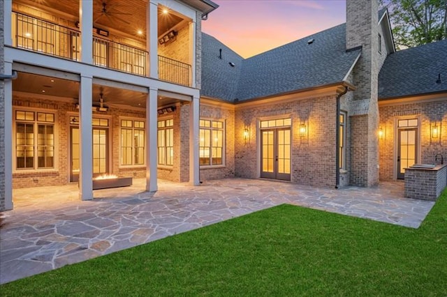 back house at dusk featuring a balcony, ceiling fan, and a patio area