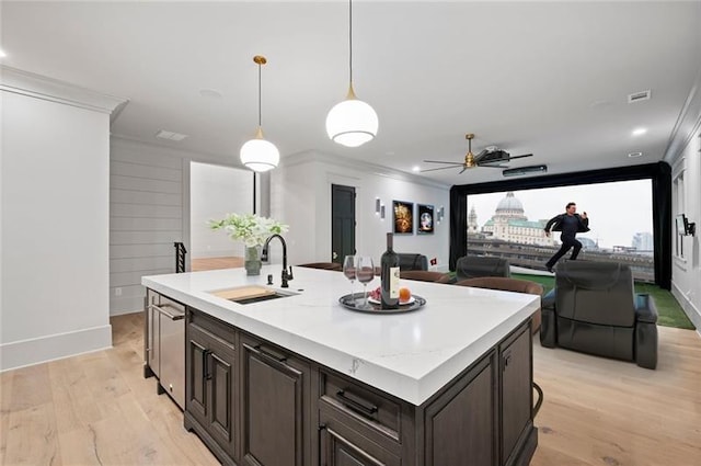 kitchen featuring dark brown cabinetry, sink, hanging light fixtures, a center island with sink, and ornamental molding