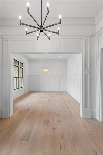 unfurnished living room featuring light wood-type flooring, an inviting chandelier, and crown molding