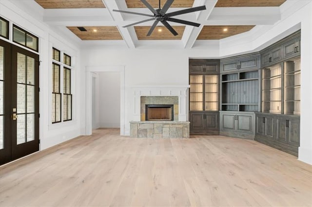 unfurnished living room featuring french doors, coffered ceiling, built in shelves, ceiling fan, and a fireplace