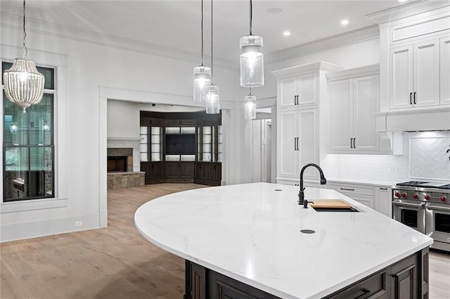 kitchen featuring white cabinets, range with two ovens, a kitchen island with sink, and sink