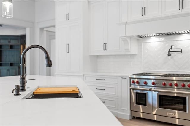 kitchen featuring decorative backsplash, white cabinetry, double oven range, and sink