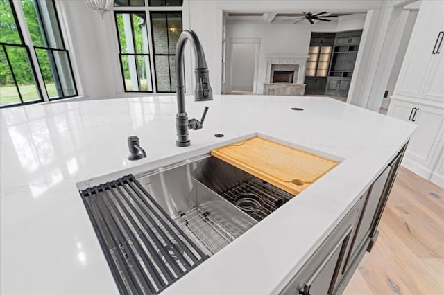 kitchen featuring white cabinets, sink, light hardwood / wood-style flooring, ceiling fan, and a fireplace