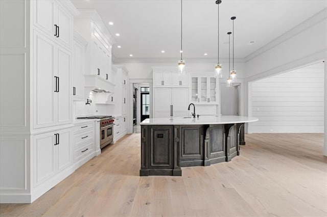 kitchen with sink, a large island with sink, decorative light fixtures, range with two ovens, and white cabinetry