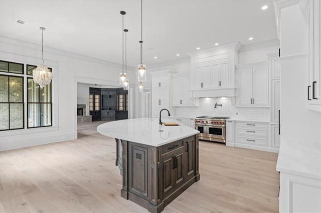 kitchen with double oven range, backsplash, white cabinets, a center island with sink, and hanging light fixtures