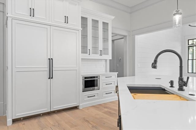 kitchen with light stone countertops, sink, pendant lighting, light hardwood / wood-style floors, and white cabinetry