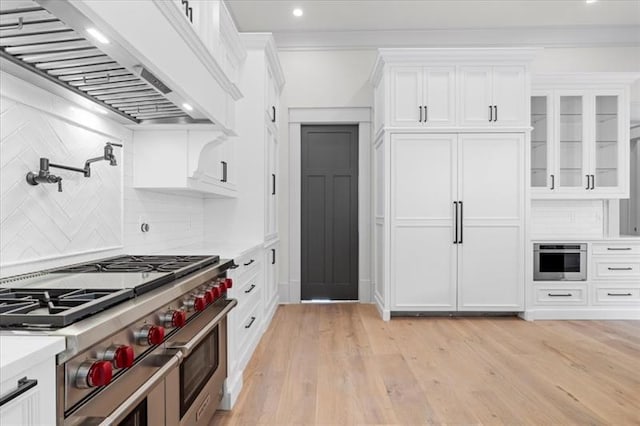 kitchen with crown molding, tasteful backsplash, white cabinetry, custom range hood, and stainless steel appliances