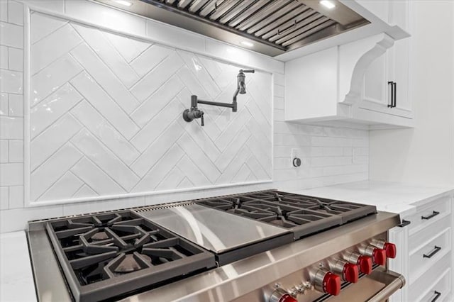 kitchen featuring white cabinets, light stone countertops, high end range, and backsplash