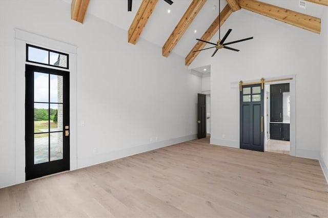 unfurnished living room with beam ceiling, ceiling fan, a barn door, high vaulted ceiling, and light hardwood / wood-style floors