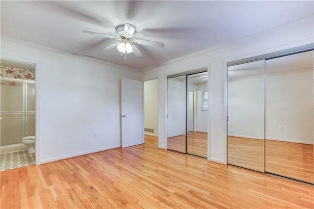 unfurnished bedroom with crown molding, ensuite bath, light hardwood / wood-style flooring, ceiling fan, and multiple closets