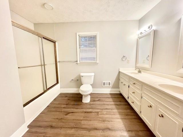 full bathroom with shower / bath combination with glass door, vanity, toilet, a textured ceiling, and hardwood / wood-style floors