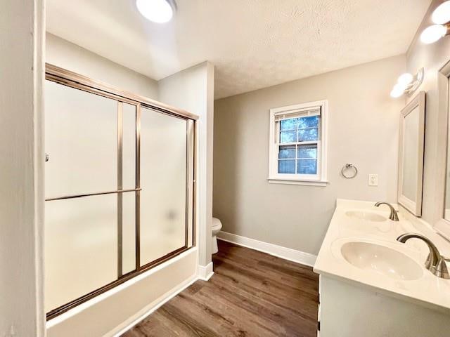 full bathroom featuring toilet, shower / bath combination with glass door, hardwood / wood-style flooring, vanity, and a textured ceiling