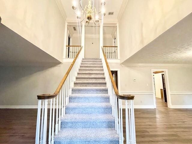 staircase with ornamental molding, hardwood / wood-style flooring, and a chandelier