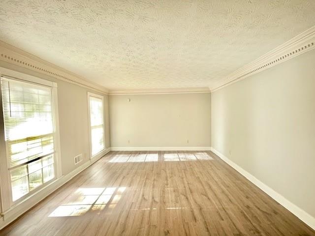 empty room featuring crown molding, hardwood / wood-style floors, a textured ceiling, and a healthy amount of sunlight