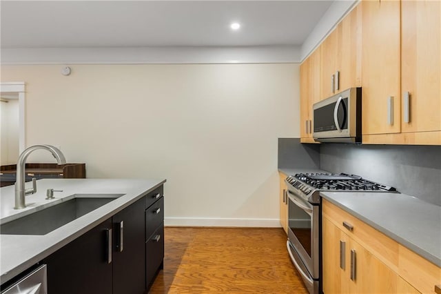 kitchen with light brown cabinets, a sink, stainless steel appliances, light wood finished floors, and baseboards