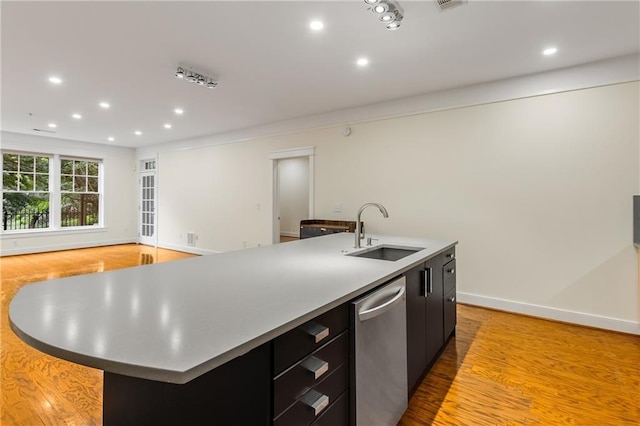 kitchen featuring stainless steel dishwasher, dark cabinetry, an island with sink, and a sink