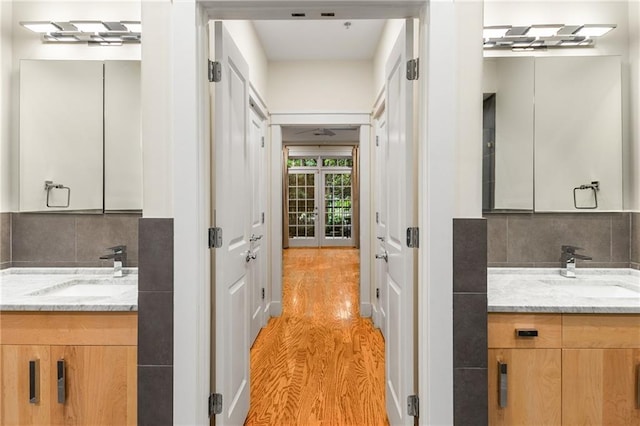 bathroom featuring two vanities, wood finished floors, backsplash, and a sink