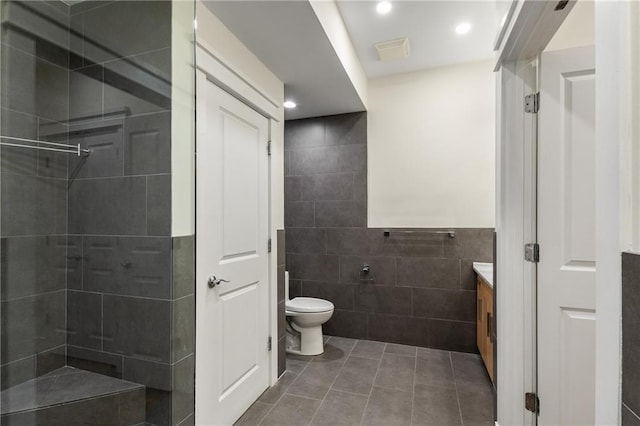 full bath featuring toilet, vanity, tiled shower, tile patterned floors, and tile walls